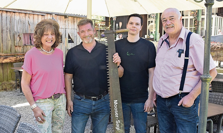 Alt und neu vereint: Heidi Mosimann (links) und Oskar «Oski» Urech (rechts) übergeben die «Moosersagi» symbolisch mit der Säge an ihre Nachfolger Sandro Boll und Martin Röthlisberger, die das Gasthaus Ende 2026 übernehmen.Bild_ Raphael Nadler